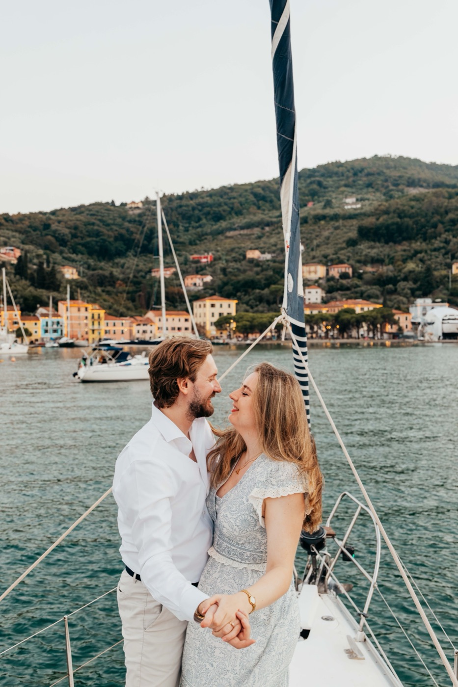 Jess and Antonio kissing at the bow, a harbour village behind them