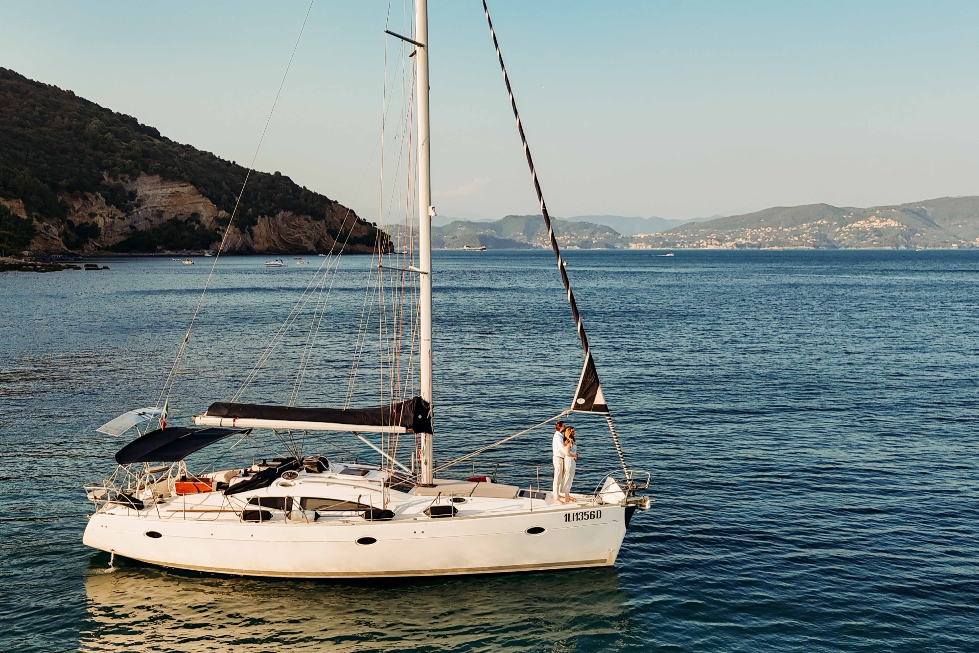 A sailboat at anchor beneath green hills on the coast