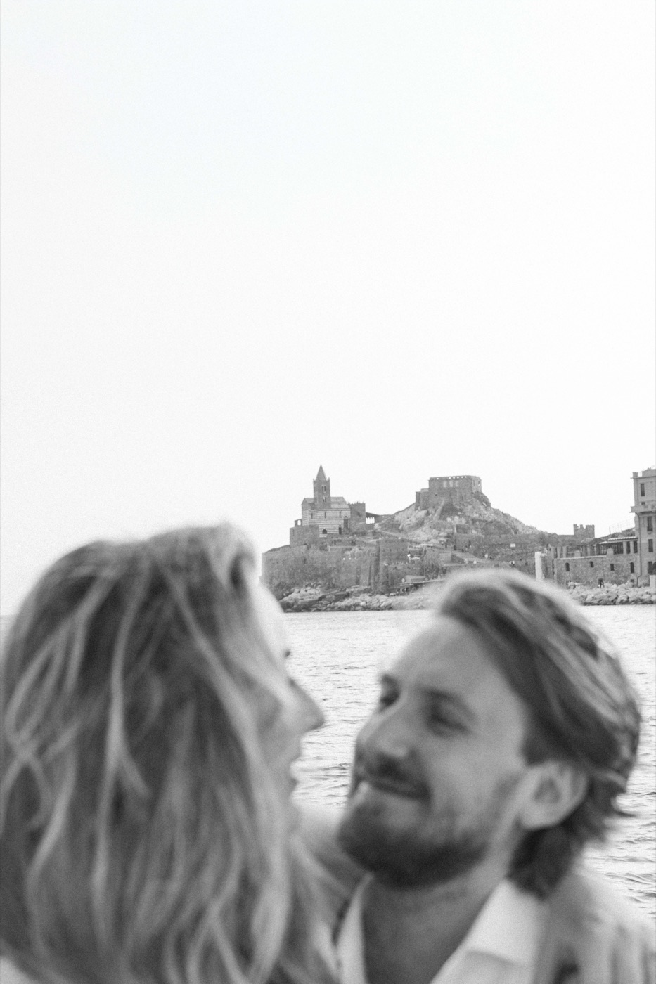 Two faces close together, a village across the water, in black and white
