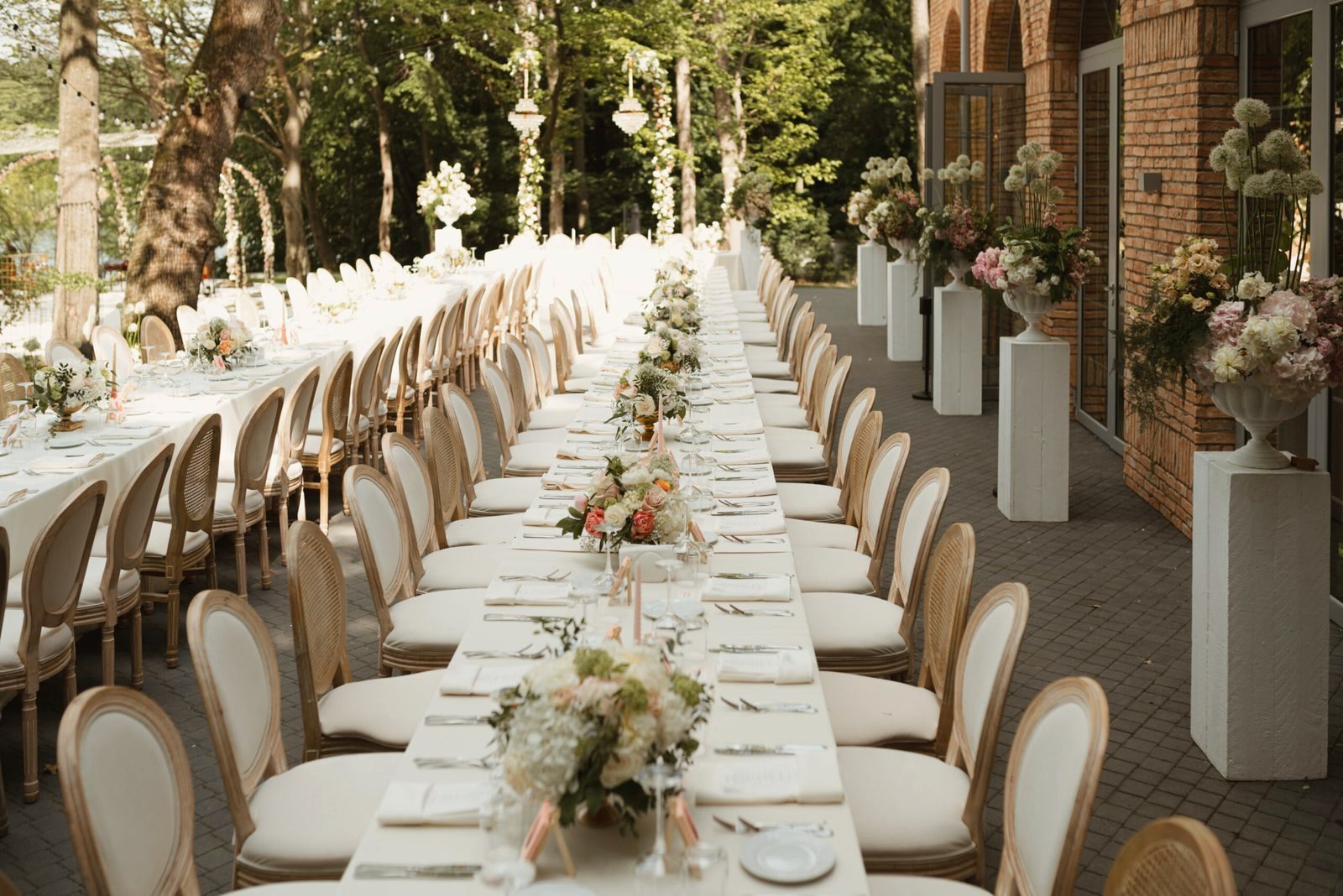 A long white banquet table with roses and chandeliers, set for dinner